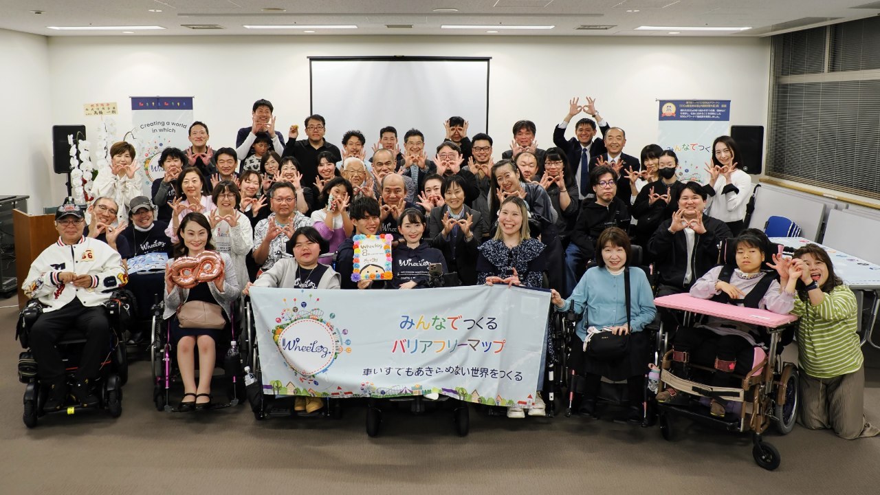 「みんなでつくるバリアフリーマップ」の横断幕を囲む、車いすユーザーを含む大勢の参加者の集合写真